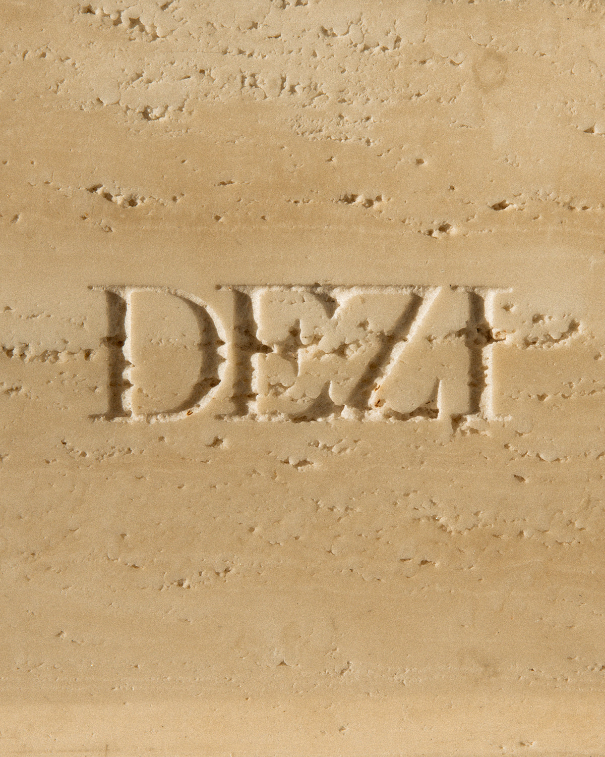 This shows a closeup of travertine stone tray with the DEZI logo carved into it. Sunlight is shining on the tray, casting beautiful shadows.