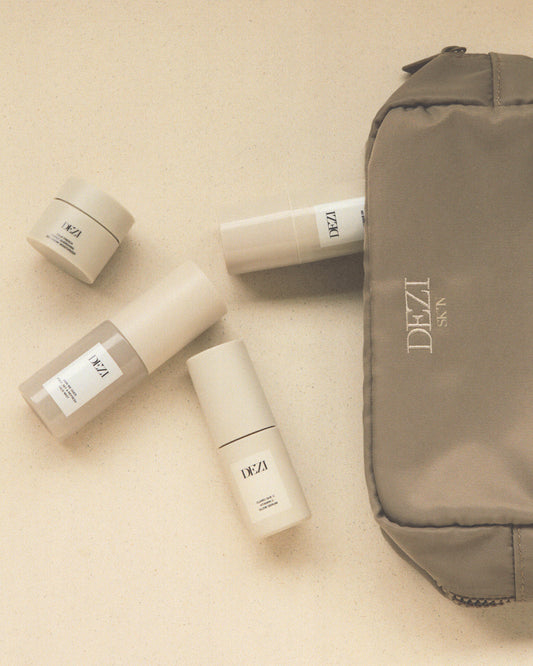 The cosmetic bag is laying on a surface and the four mini travel size skincare products are spilling out of it. 