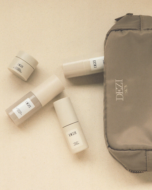 The cosmetic bag is laying on a surface and the four mini travel size skincare products are spilling out of it.