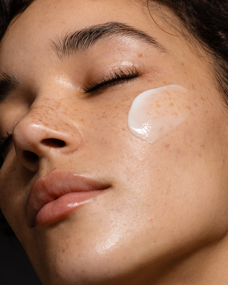 Model's face with a swatch of the moisturizer on her cheek.