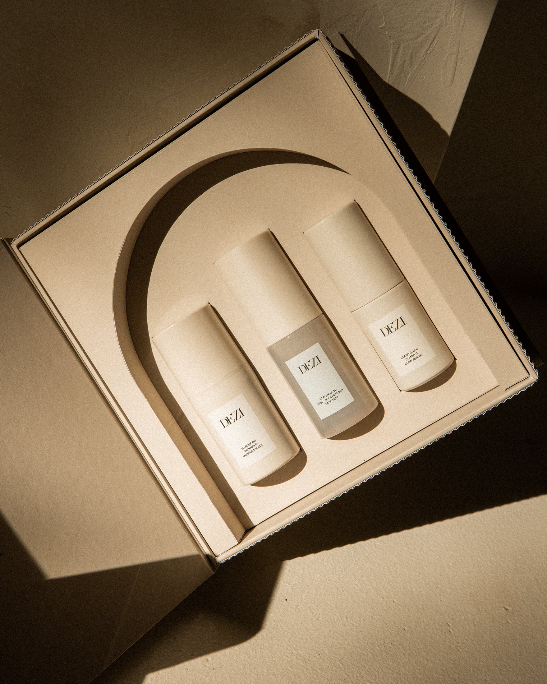 This shows three DEZI SKIN travel size products in the custom box. They are sitting in a tray that is shaped like an arch, inspired by architecture. 