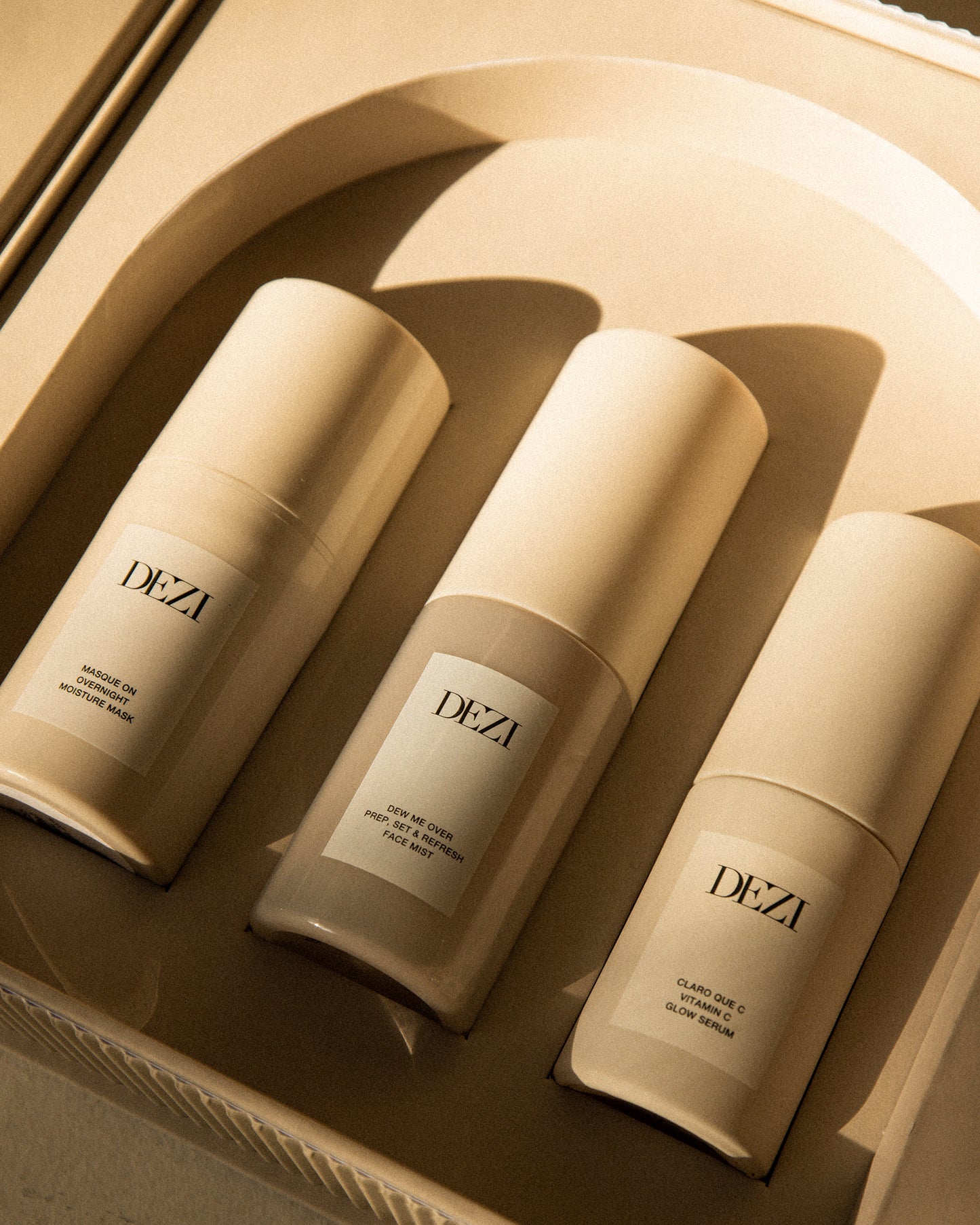 This shows three DEZI SKIN travel size products in the custom box. They are sitting in a tray that is shaped like an arch, inspired by architecture.