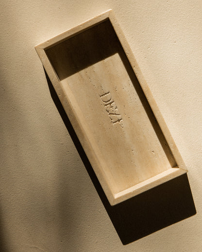 This shows a travertine stone tray with the DEZI logo carved into it. Sunlight is shining on the tray, casting beautiful shadows. 